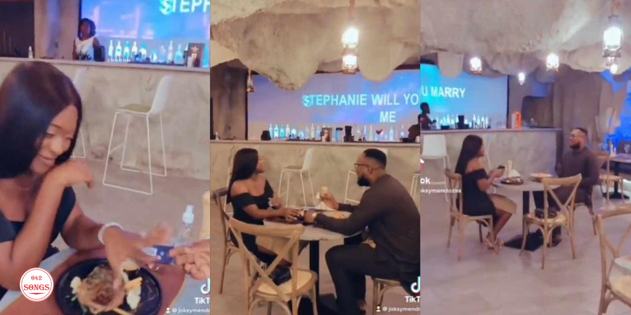 Reactions as man sits on chair to propose to girlfriend in restaurant